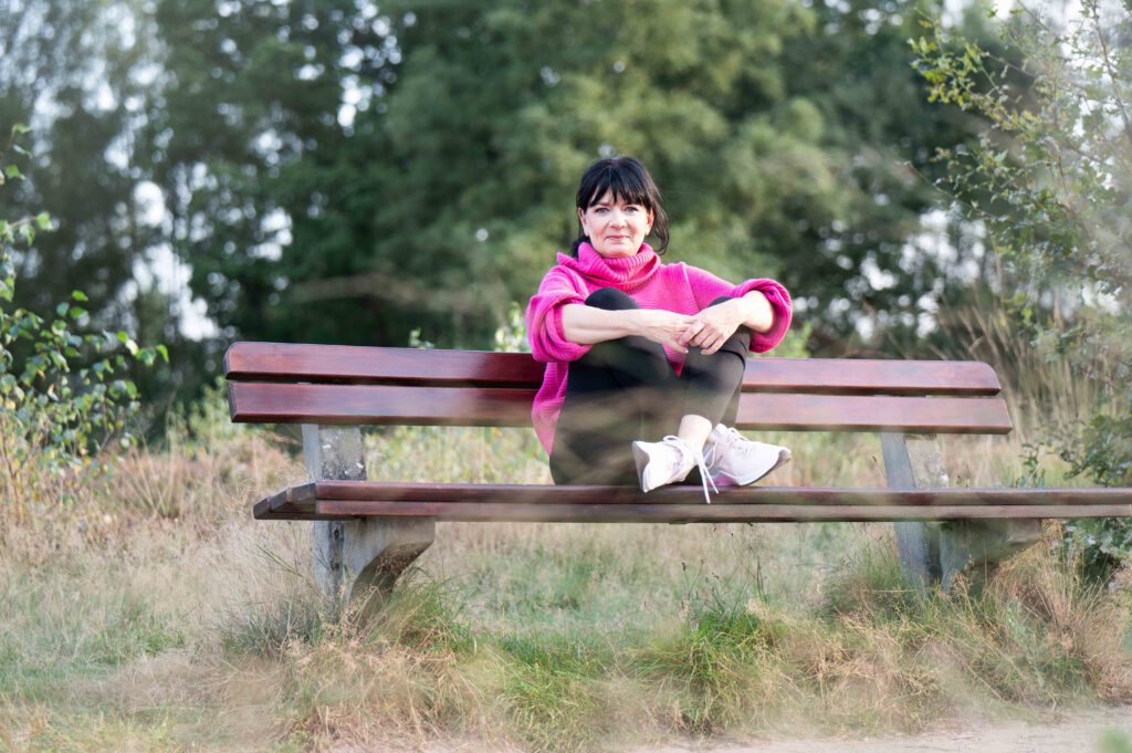 Frau in pinkem Pulli auf Bank in der Natur sitzend