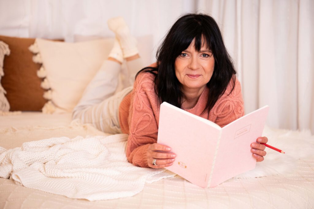 Frau mit Notizheft lächelnd auf Bett liegend