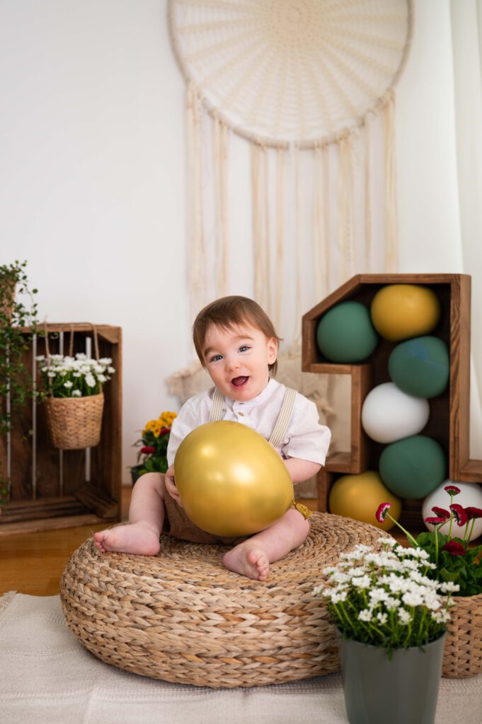 Portrait von kleinem lachendem Jungen mit Luftballon beim Fotoshooting zum 1. Geburtstag