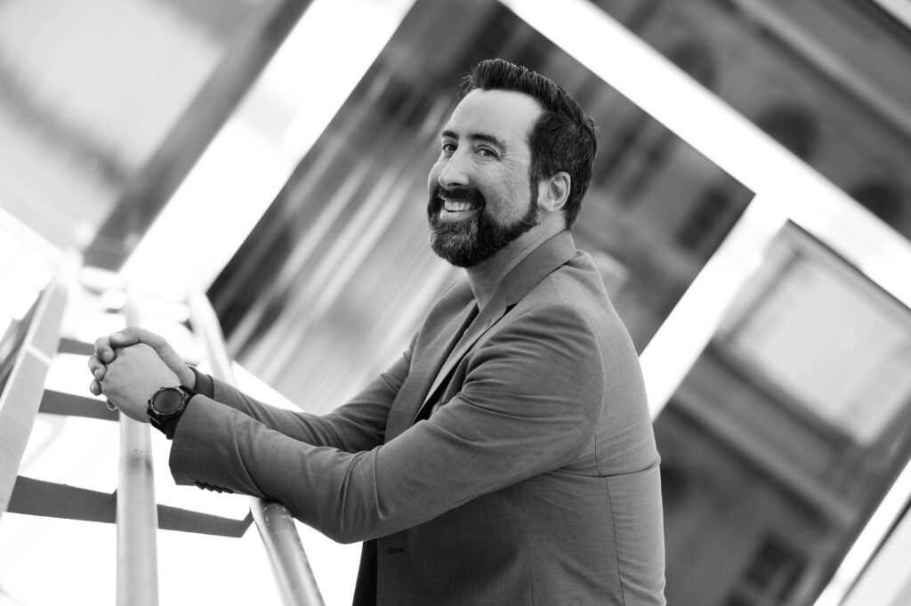 Mann an ein Geländer gelehnt vor Glasfassade beim Business-Shooting