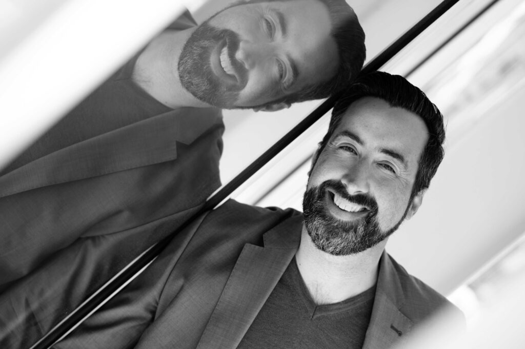 lachender Mann an Glasfassade gelehnt mit Spiegelbild beim Business-Shooting